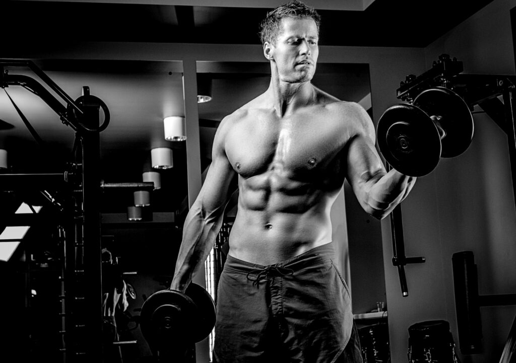 muskularny-mezczyzna-shirtless-robi-biceps-cwiczenia-z-hantlami-w-klubie-silowni